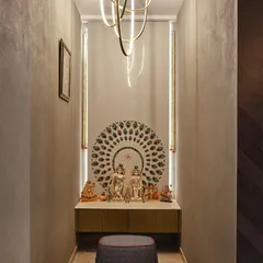 A compact and elegant pooja space featuring a marble platform, a peacock-feather-inspired backdrop, and warm vertical lighting. This design shows how a serene prayer corner can be created even in a smaller area.