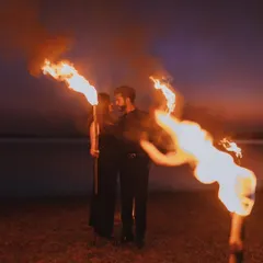 A dramatic pre-wedding shoot at dusk, using fire torches to create a powerful and romantic atmosphere by the water.