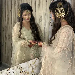 A quiet moment of reflection for the bride. Her hair is styled in soft waves with a traditional passa and maang tikka, perfectly complementing her elegant outfit.