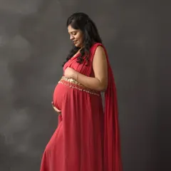 A classic profile portrait of an expecting mother in a vibrant red gown. The dark, textured backdrop makes the color pop, emphasizing the beauty of the baby bump.