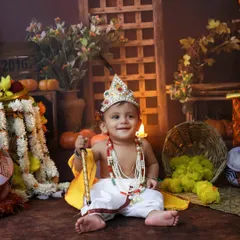 A smiling baby Krishna sits among festive decorations, holding his flute. We aim to capture the innocent and playful nature of Kanha in these special photoshoots.