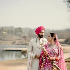 A powerful and regal portrait of a Sikh couple by the lakeside. The groom holding the kirpan and the bride's magnificent pink lehenga create a picture of royal elegance.