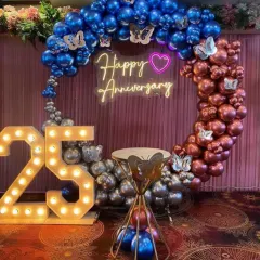 A grand 25th anniversary celebration setup. This decoration features a ring arch with metallic blue, silver, and rose gold balloons, a neon sign, and large light-up numbers.
