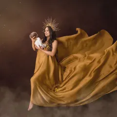 A goddess-like portrait of a mother holding her newborn, wearing a flowing golden gown and a sunburst crown.