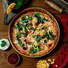 A top-down shot of a colorful vegetable pizza in a brass pan. The rich colors of the toppings and the rustic presentation make it look like a gourmet, artisanal creation.
