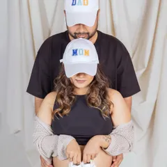 A fun and modern way to announce your new roles. This couple wears matching "Mom" and "Dad" caps, with the mom-to-be holding a tiny pair of baby shoes over her bump for a playful and casual maternity photo.