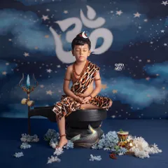 In deep meditation, this little one embodies the calm and powerful presence of Lord Shiva. The setup includes a Shivling, Trishul, and a starry night backdrop to create a truly divine atmosphere.