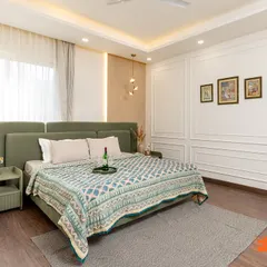This serene master bedroom combines a soft green upholstered bed with classic white wall molding. The elegant pendant lighting and sheer curtains create a tranquil and airy atmosphere.