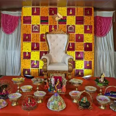 This Seemantham setup showcases a vibrant marigold checkerboard backdrop in yellow and magenta. In the foreground, you can see the detailed arrangement of sweets, fruits, and decorative dolls.