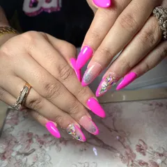 A bold and glamorous set featuring hot pink stiletto nails. The design is accented with a glitter fade and large, multi-shaped iridescent crystals for maximum impact.