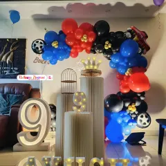 A cool race car themed party for a 9th birthday. The setup includes a balloon arch in red, blue, and black, with car wheel details and a large light-up number '9'.
