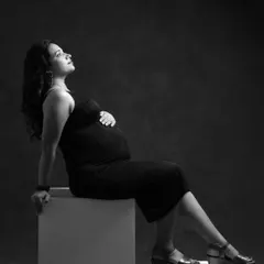 An elegant black and white portrait emphasizing light and shadow. The mom-to-be looks up thoughtfully, her hand on her bump, creating a powerful and contemplative image.