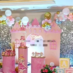 A dreamy princess castle stage setup in shades of pink, silver, and gold, featuring a sequin wall and multiple pedestals for cakes and desserts.