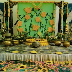A stunning Haldi stage set by a serene pool. The backdrop features a custom pichwai-style painting with 3D marigold lotuses, surrounded by traditional brass pots and floral arrangements. The water is filled with floating flowers, adding to the magic.