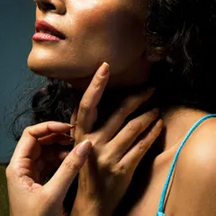 A close-up portrait focusing on texture and form. The soft light caresses the subject's skin, highlighting the elegant lines of her neck and hands in a moment of quiet grace.
