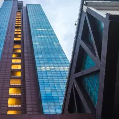 A low-angle view of The Ruby in Dadar, emphasizing its impressive scale and structural design. The exposed truss work and the contrast between the solid podium and the glass curtain wall showcase the technical precision and bold aesthetics of our commercial architecture.