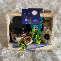 A thoughtful Raksha Bandhan hamper designed for a brother. This gift includes post shave balm, Ferrero Rocher chocolates, sugar free sweets, and a "Happy Raksha Bandhan" card, all arranged in a rustic wooden crate.