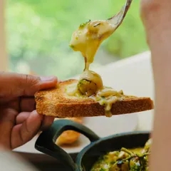 A guest enjoying our oven-roasted Kumaoni grapes with melted hot brie on sourdough toast. This dish is a perfect example of our philosophy of pairing exceptional regional ingredients with artisanal products.