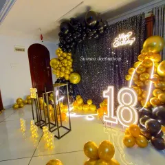 A glamorous 18th birthday party with a black and gold theme. The decor includes a black shimmer wall, a neon sign, large '18' marquee numbers, and a matching balloon garland.