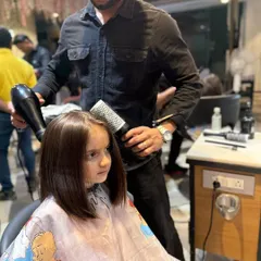 A young client getting a sleek bob haircut. Our stylist is carefully blow-drying her hair, showing the gentle and professional approach we take with our 'Kool Kid' clients.
