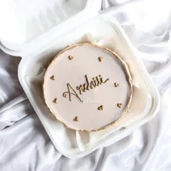 A simple and elegant bento cake with a custom name in gold script, surrounded by tiny hearts. Perfect for a minimalist celebration.