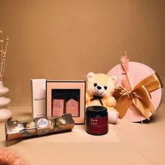 The 'Sweet Serenity' hamper is a bundle of love and comfort. It includes a cuddly teddy bear, Ferrero Rocher chocolates, a scented candle, and a perfume and lotion set.