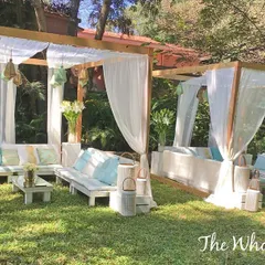 I created these custom-built wooden cabanas with flowing white drapes to provide a relaxed and breezy lounge area for an outdoor party. The space is furnished with comfortable seating, soft blue and white cushions, and rustic lanterns to establish a chic, beach-inspired vibe.