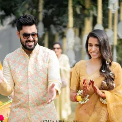 The happy couple enjoying their sunlit Haldi ceremony. The groom wears a pastel printed jacket, and the bride is radiant in a yellow saree, perfectly complementing the traditional and natural decor.