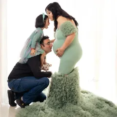 A beautiful family portrait full of love. The dad gives his daughter a shoulder ride while she gives her mom's baby bump a sweet kiss.