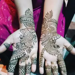 A pair of hands with matching Arabic-style designs. The patterns are not identical but complement each other beautifully, featuring bold lines and shaded florals.