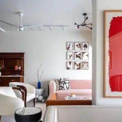 A view through an archway reveals how we layer color and texture. The soft pink sofa provides a gentle pop of color, balanced by modern art and sculptural white and black armchairs, creating a dynamic yet cohesive living space.