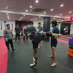 In our beginner classes, we break down the fundamentals. A coach holds pads for a student, ensuring they develop the correct form and power for a foundational kickboxing roundhouse kick.