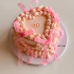 A beautiful heart-shaped cake in a soft pink hue, decorated with classic vintage Lambeth piping and delicate organza ribbons. This design is perfect for celebrating a 20th birthday in style.