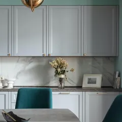 A sophisticated kitchen and dining area with PU-finished grey cabinets, a marble backsplash, and plush teal dining chairs.
