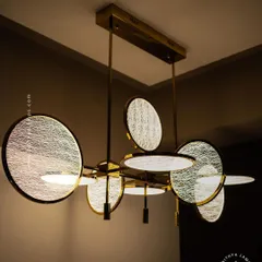 Modern artistry meets functional lighting in this unique chandelier. Featuring textured, disc-shaped diffusers on a brass frame, it provides warm, even light, making it a perfect statement piece over a contemporary dining table.