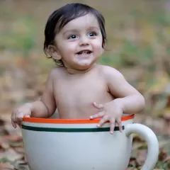 A happy baby boy with a big smile, posing in our giant teacup prop during an outdoor session among autumn leaves.