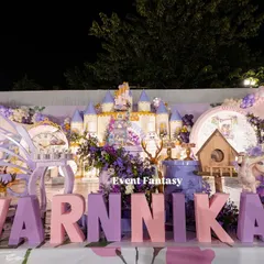 A full stage view of Varnnika's fairyland, a stunning setup in shades of purple and pink. It features a large castle backdrop, oversized name blocks, fairy dolls, and whimsical butterfly wing props.
