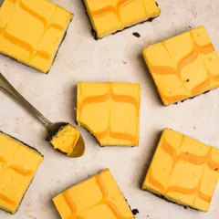 A beautiful flat lay of mango cheesecake bars. The vibrant yellow and clean composition make this a bright, summery shot that emphasizes the dessert's smooth texture and beautiful marbled pattern.