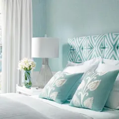 A delicate, light blue textured pattern on the wall complements the geometric headboard in this bedroom. This technique adds subtle visual interest without overwhelming the serene and calming atmosphere of the space.
