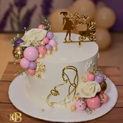 A beautiful and elegant cake to celebrate a baby shower. This design features a gold acrylic silhouette of a mother-to-be, a "Baby Shower" topper, and a cascade of pink, purple, and gold spheres.