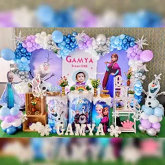 A magical winter wonderland with our Disney's Frozen themed party decor. This setup for Gamya's first birthday includes a full balloon arch in shades of blue, purple, and silver, with character cutout's of Elsa, Anna, and Olaf.