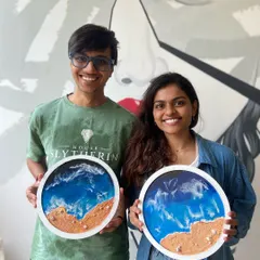 A smiling couple holding their matching resin beach art pieces. Our workshops are designed to be fun and collaborative, making them a great activity for friends and partners.
