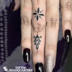 Elegant fine-line tattoos on the fingers, including a starburst and a delicate ornamental design.