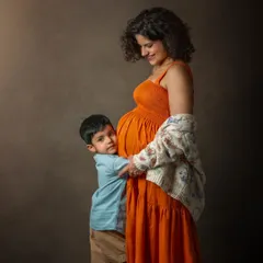 This studio maternity portrait captures the sweet bond between a mother and her son as they await a new arrival. The protective hug and gentle expression tell a story of love and excitement.