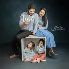 Celebrating a "two" big milestone. This family portrait captures the parents with their adorable twins, who are sitting in a box, for a pre-birthday photoshoot.