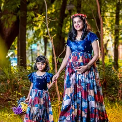 A mother and daughter in matching dresses during a maternity photoshoot in the woods. This beautiful outdoor portrait captures the special connection they share as they await the new family member.