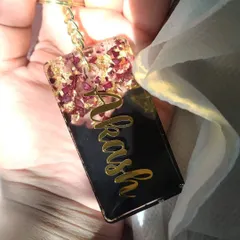 This keychain is a beautiful way to preserve a memory. I used crushed rose petals and gold flakes at the top of this rectangular keychain, with the name 'Akash' in a flowing gold script on a solid black background.