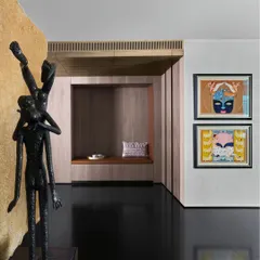 A close-up of a sculpture by Radhakrishnan Sreeman set against a natural stone wall by Odyssey. The image highlights the contrast between the smooth, dark bronze of the sculpture and the rough, organic texture of the stone.