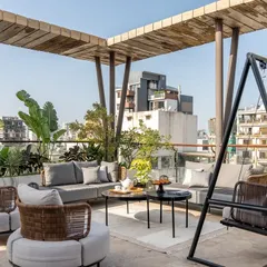 A view of the terrace seating area, complete with comfortable sofas, a modern swing, and lush planters. It’s an extension of the indoor lounge, designed for both relaxation and entertainment against the city skyline.