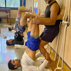 Here, a coach assists a tennis player in a supported shoulder stand variation using the wall. This pose is excellent for recovery, calming the nervous system, and improving circulation after intense training.